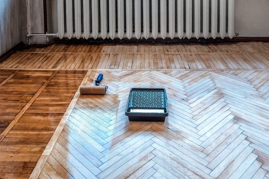R&eacute;novation de parquet en cours dans une pi&egrave;ce d'appartement ancien avec radiateur fonte