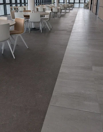 Salle de restauration moderne avec tables et chaises en bois clair disposées dans un espace lumineux aux grandes baies vitrées